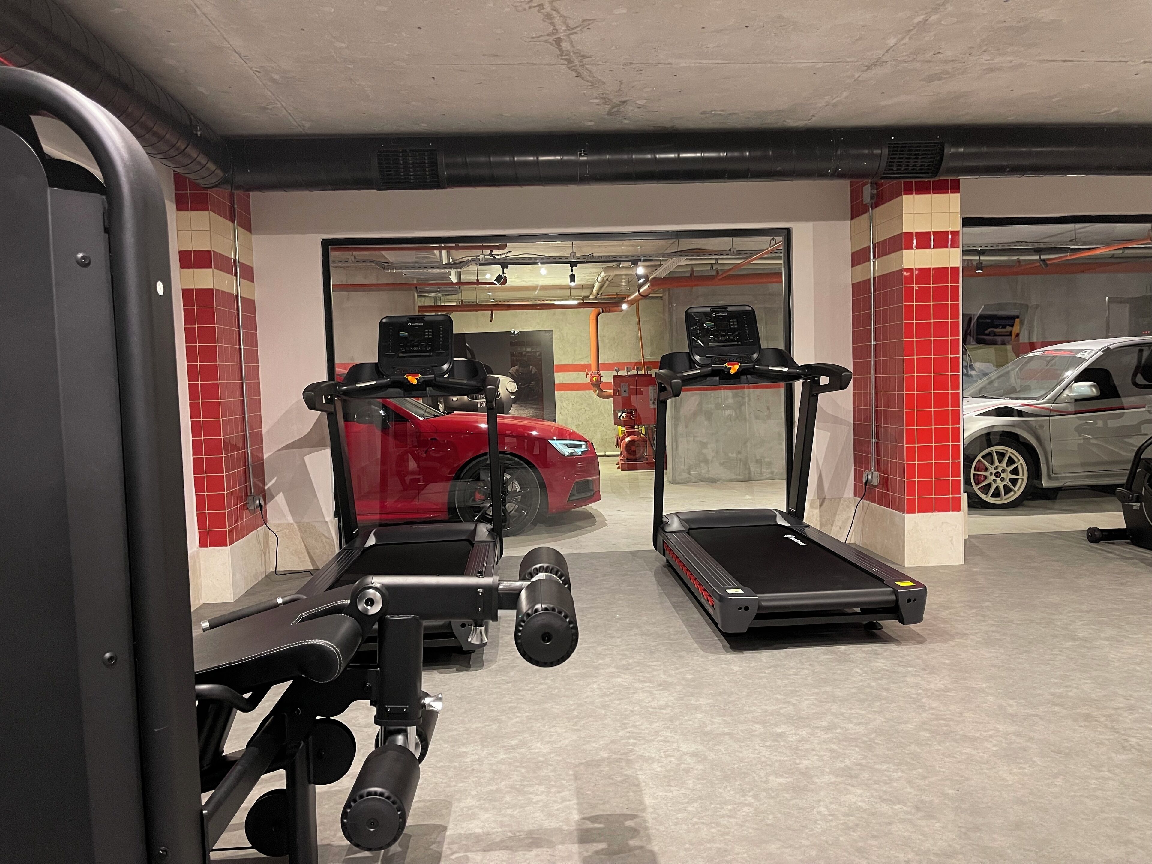 A gym with treadmills, a bench press, and a red sports car in the background.