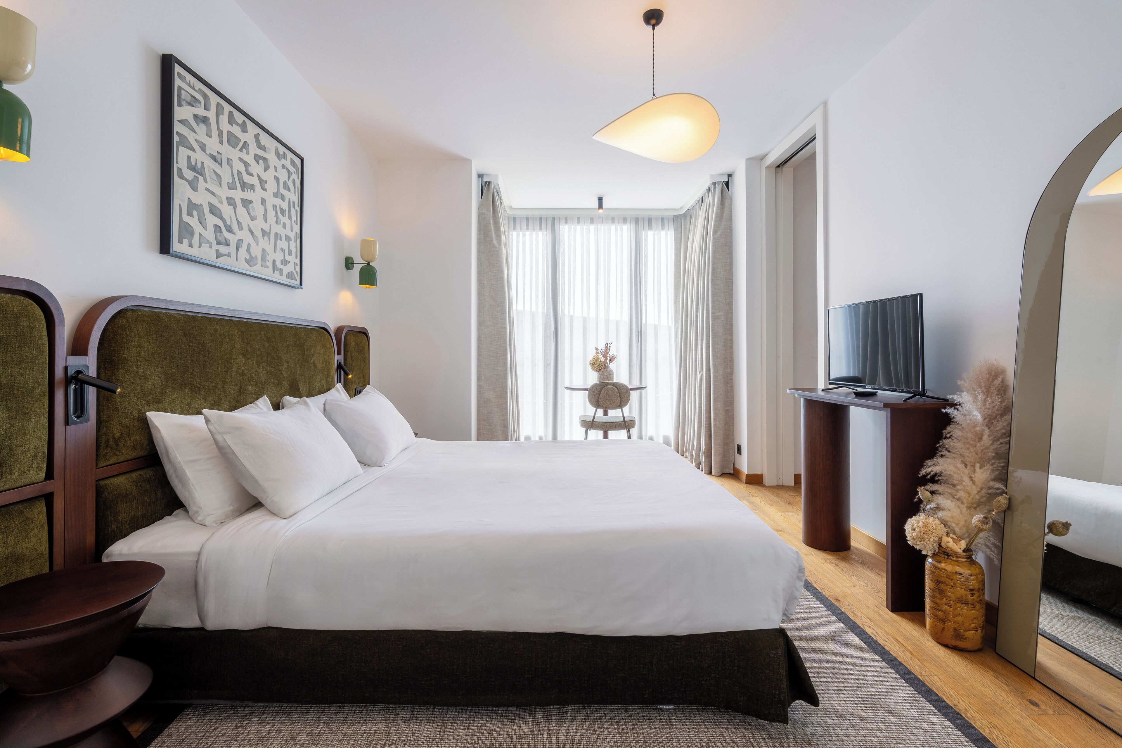 A modern hotel room with a large bed, a desk, a television, and a decorative vase.
