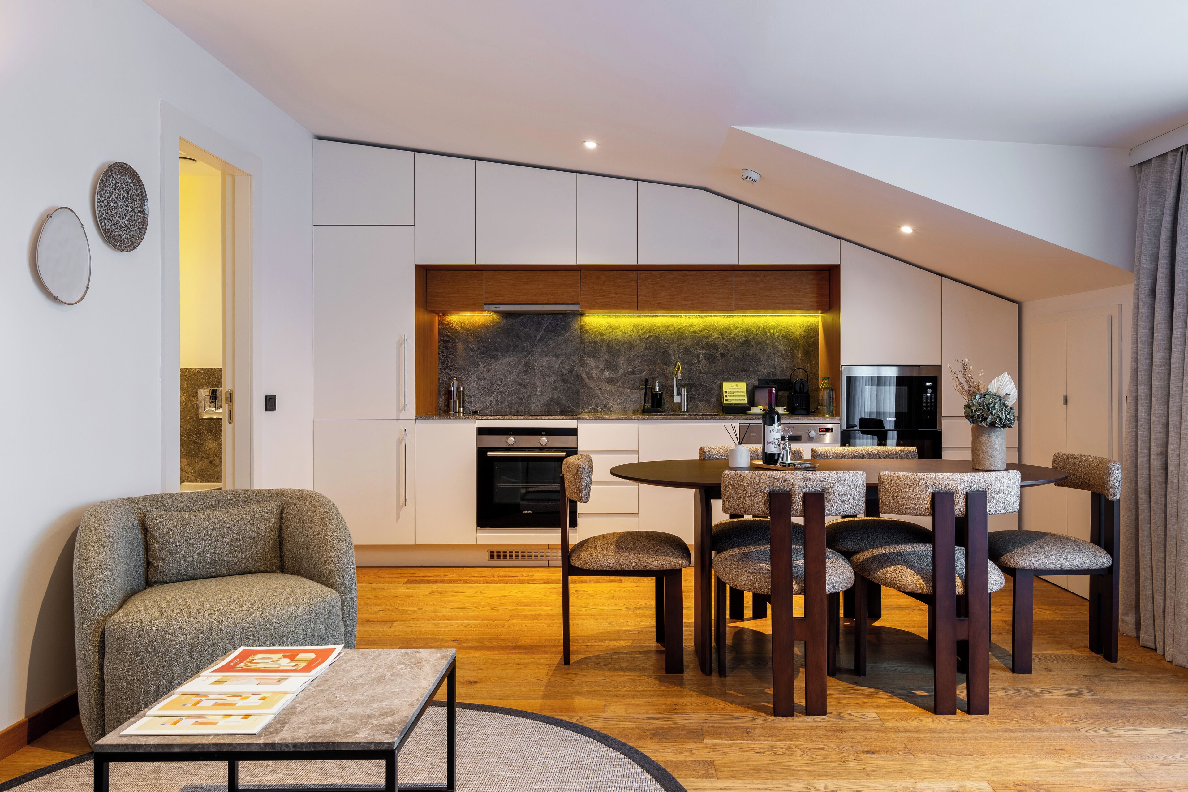 A modern kitchen with a built-in oven, microwave, and a dining area with a round table and six chairs.