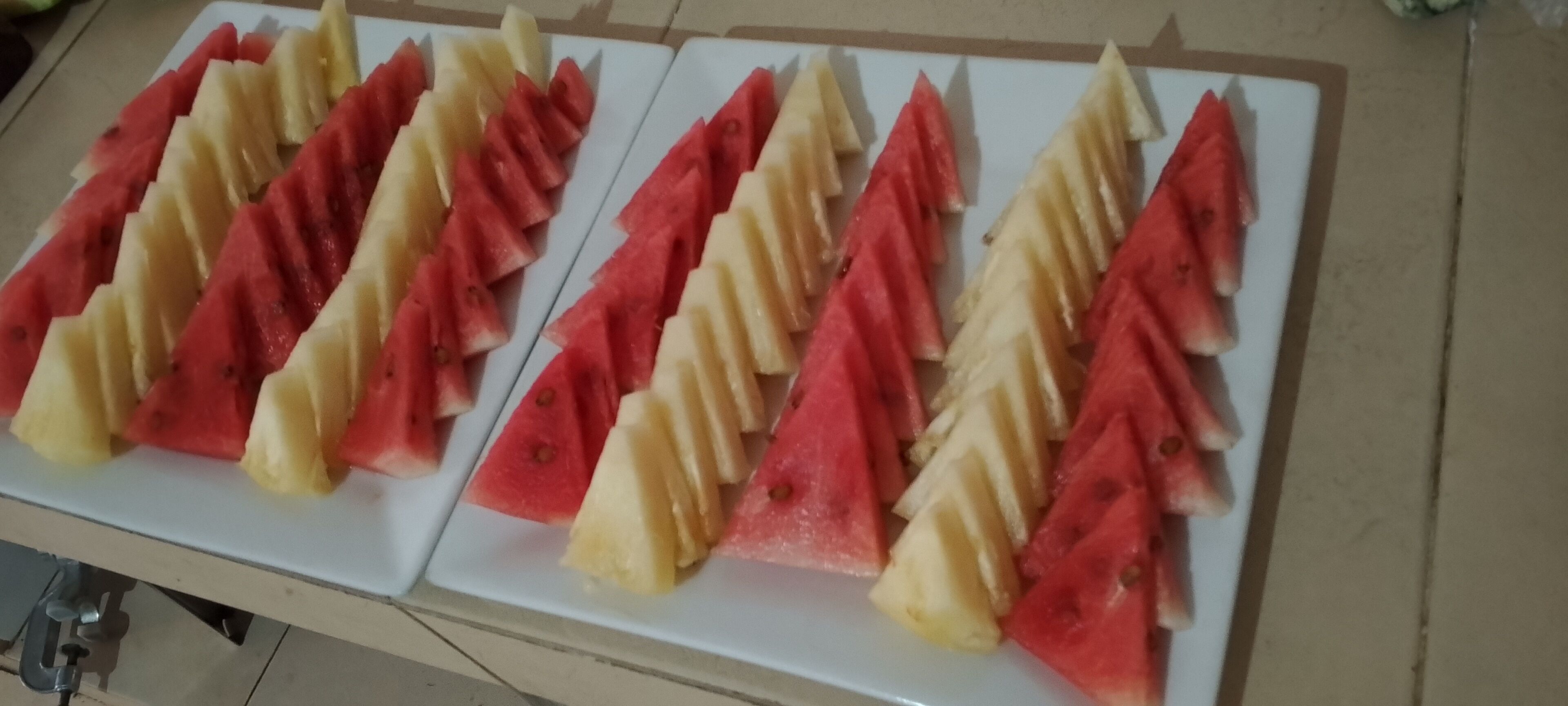 Two white cutting boards with sliced watermelon and cantaloupe arranged in rows.