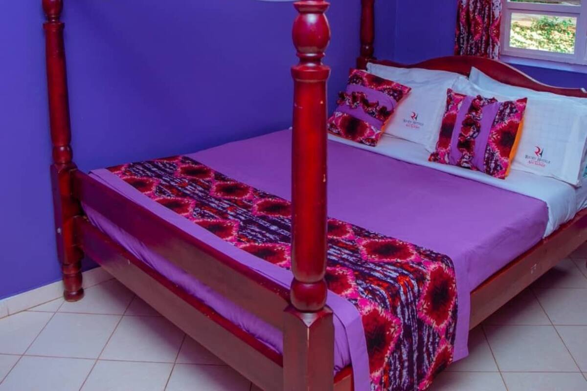 Ein Bett mit Baldachin, eine violette Wand und ein Fenster mit Vorhängen.