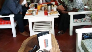 A group of people seated around a table with breakfast items, in a room with a green wall and framed pictures. - Richy Hotels and Safaris (Mbale)
