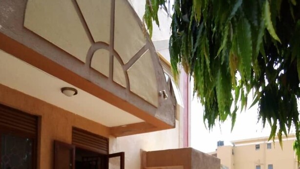 An outdoor seating area with a round table and four chairs, a green metal railing, and a building with a beige facade and a sign that reads "Royal Palm Plaza." - Richy Hotels and Safaris (Mbale)