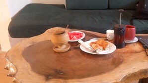 A wooden table with a plate of food, a coffee maker, a laptop, and a bag in a room with a green couch. - Richy Hotels and Safaris (Mbale)