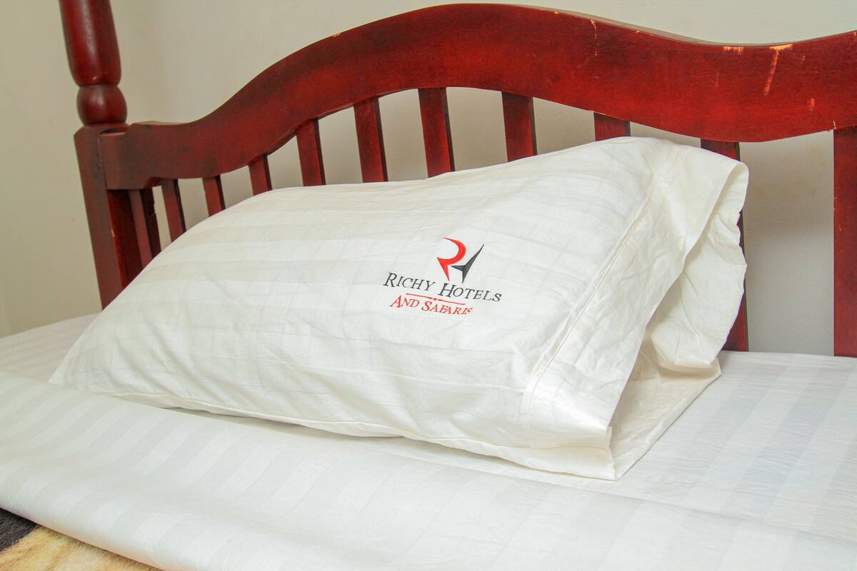 Ein Bett mit einem Kopfkissen, das das Logo von Richy Hotels und Safari zeigt.