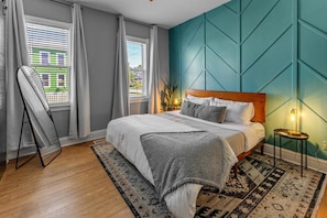 Una camera da letto con un letto, una ventola, un comodino, una lampada e vista su un edificio dalla finestra.