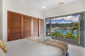 A hotel room with a bed, a view of a marina, and a balcony with a pool.