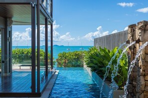 A swimming pool with a view of the ocean and boats, surrounded by greenery and a stone wall. - Anusara - Airlie Beach (Airlie Beach)