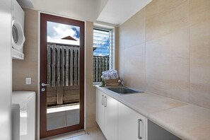 Cocina compacta con lavadora incorporada, una ventana con persianas y vistas al exterior.