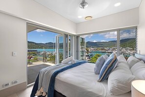 Un dormitorio con cama, almohadas y vistas a un puerto deportivo y montañas.