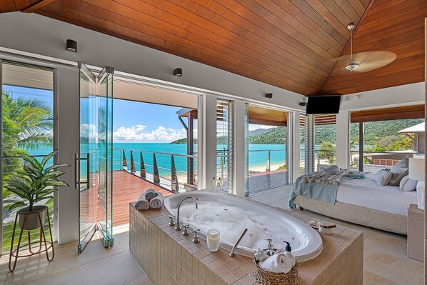 Un baño moderno con una bañera grande, una ducha con mampara de vidrio y vistas al mar.