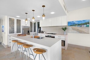 Eine moderne Küche mit einer großen Kochinsel, Barhocker, Pendelleuchten und einem Gemälde an der Wand.