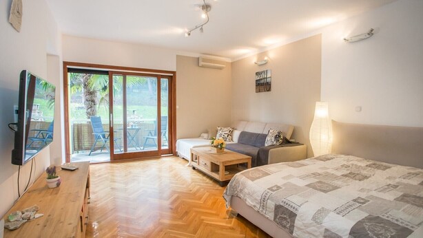 Una habitación amplia con una cama grande, un sofá, una mesa de madera y un televisor montado en la pared.