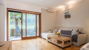Una sala de estar moderna con un sofá, una mesa de centro y un gran ventanal corredero que da a un área exterior con sillas y una mesa.