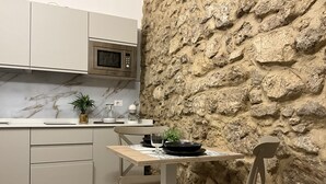 A compact kitchen with a stone accent wall, a microwave, a coffee maker, and a dining table with chairs. - Rua 39 fine apartments (Syracuse)