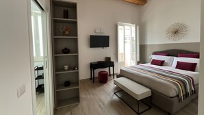 A bedroom with a bed, a TV, a shelf, and a bench. - Rua 39 fine apartments (Syracuse)