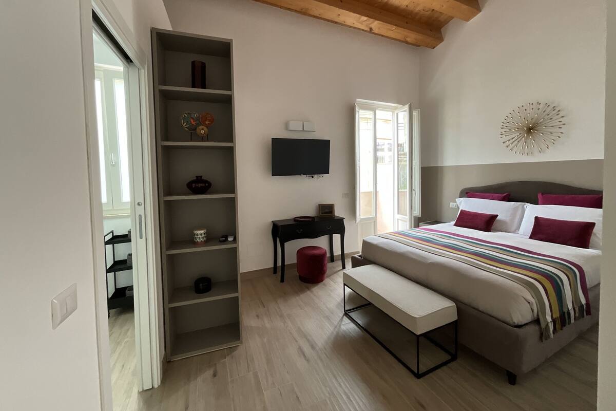 Une chambre à coucher avec un lit, une télévision, une étagère et un banc.