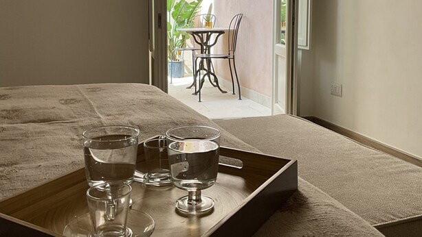A bedroom with a wooden tray holding glasses of water, a bed, and a view of an outdoor patio with a table and chairs. - Rua 39 fine apartments (Syracuse)