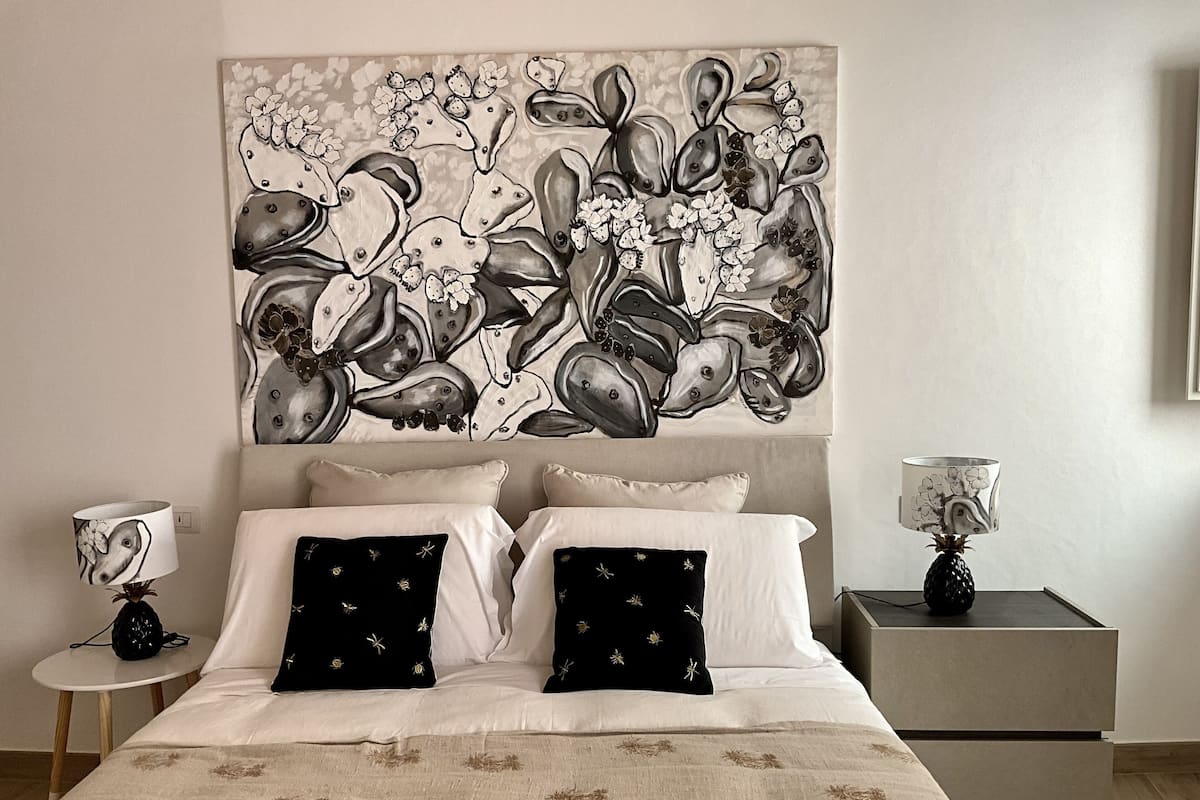 Une chambre à coucher avec une grande peinture abstraite au mur, un lit avec des oreillers blancs et noirs, une table de chevet avec une lampe et une commode avec une lampe.