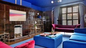 Ein Zimmer mit großem Fenster, Kamin, einem roten Sessel und einem blauen Sofa.