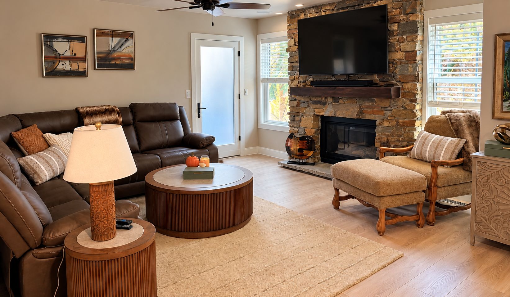 A living room with a stone fireplace, leather sofas, a round coffee table, and a television mounted on the wall.