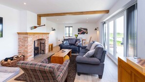 A spacious living room with a fireplace, a sofa set, and a large window offering a view. - The Holt (Stamford)