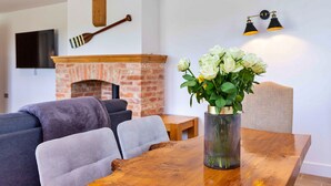 A dining area with a wooden table, a vase of white flowers, a brick fireplace, and a modern light fixture. - The Holt (Stamford)