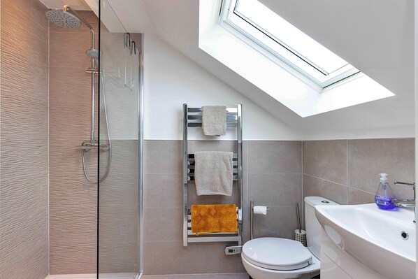 A modern bathroom with a skylight, a glass shower enclosure, a toilet, and a sink with a soap dispenser.