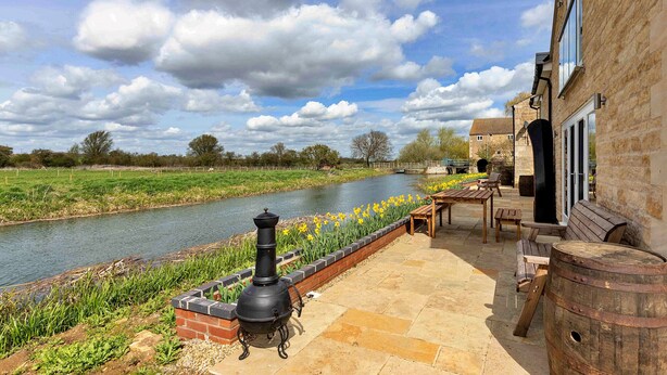 A riverside patio with a brick wall, outdoor seating, and a chimney. - The Holt (Stamford)