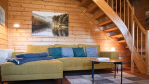 Una habitación acogedora con techo de madera, un sofá con cojines, una mesita y un cuadro de un lago.