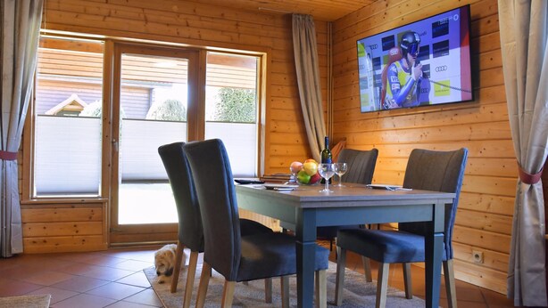Una cabaña de madera con comedor, que incluye una mesa, sillas y un televisor mostrando un evento deportivo.