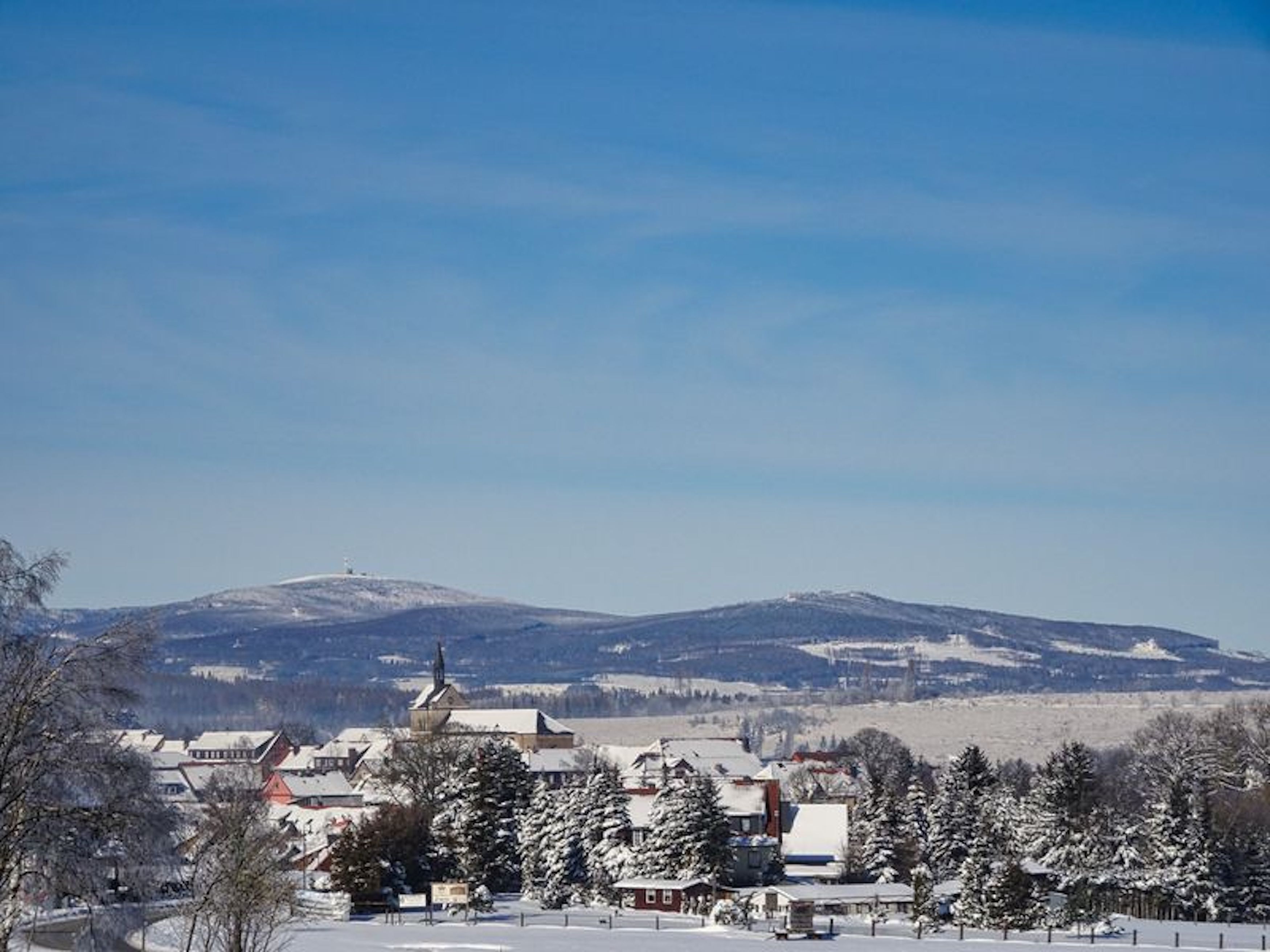 Ein verschneites Dorf mit traditionellen Gebäuden und einer Kirche, umgeben von Bergen.