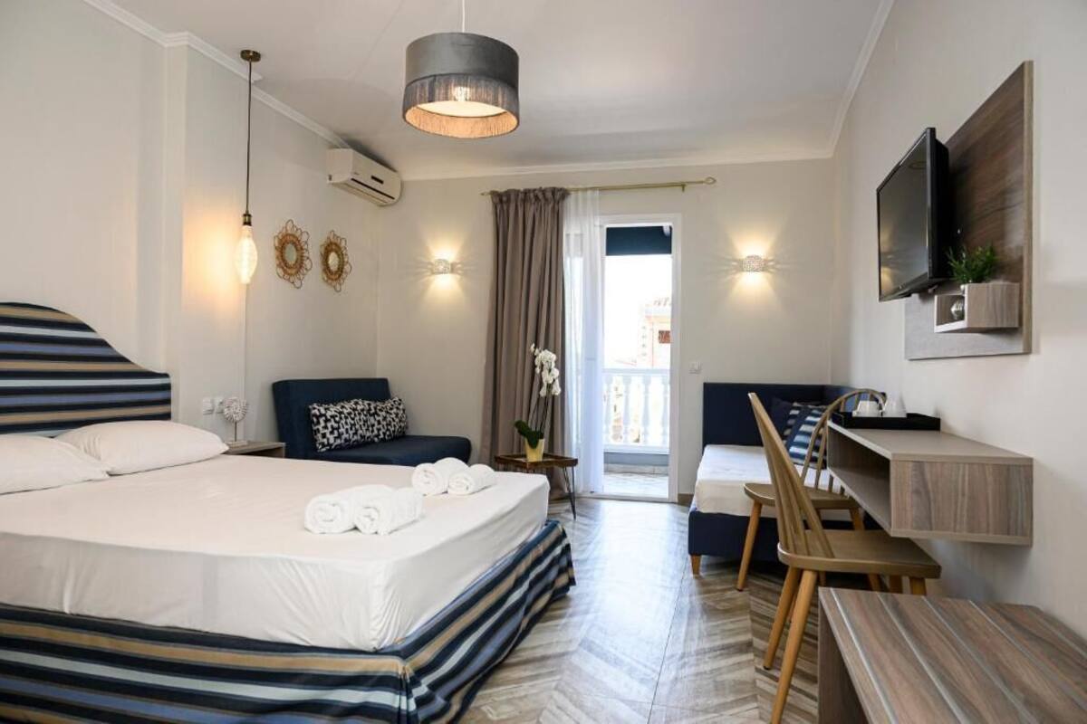 A hotel room with a large bed, a desk, a chair, a television, and a balcony with curtains.