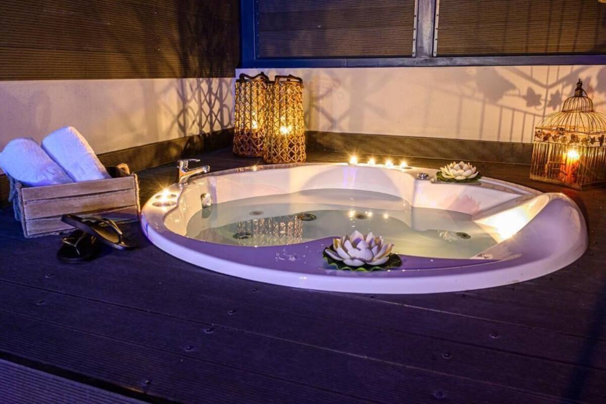 A hot tub with candles and a lotus flower decoration, surrounded by wooden furniture and decorative lanterns.