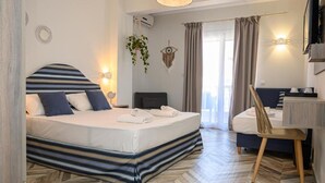 A modern hotel room with a large bed, a desk, and a chair. There is a window with curtains, a wall-mounted TV, and a plant hanging from the ceiling. - Parthenon Art Executive Wing (Katerini)