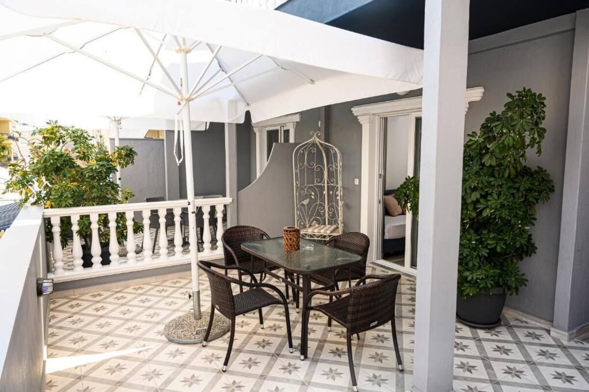 A patio with a table and chairs, a white railing, and potted plants.