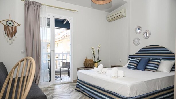 A hotel room with a bed, a chair, a small table with a plant, and a view of the outside. - Parthenon Art Executive Wing (Katerini)