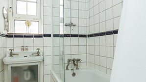 A bathroom with white tiles, a glass shower enclosure, a white sink with two faucets, and a window with a flower. - Convenient 2 Bedroom Apartment in Central London (London)
