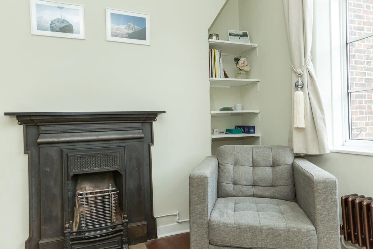 A living room with a fireplace, a grey armchair, and a bookshelf.