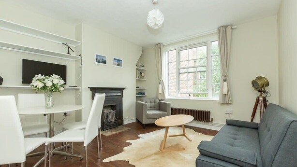 A modern living room with a fireplace, a grey sofa, white chairs, and a dining table. - Convenient 2 Bedroom Apartment in Central London (London)
