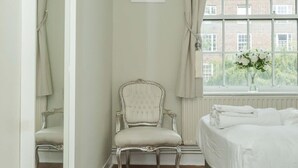 A bedroom with a bed, a chair, a window with a view of buildings, and a mirror. - Convenient 2 Bedroom Apartment in Central London (London)
