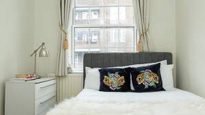A bedroom with a large window, a white dresser, a fluffy white bedspread, and two decorative pillows with tiger designs. - Convenient 2 Bedroom Apartment in Central London (London)