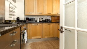 A kitchen with wooden cabinets, a gas stove, a microwave, and a coffee maker. - Convenient 2 Bedroom Apartment in Central London (London)