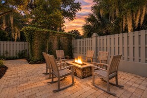 An outdoor patio with a fire pit, wooden chairs, and a brick floor.
