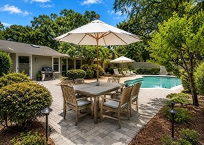 A backyard with a pool, patio furniture, and a barbecue area.