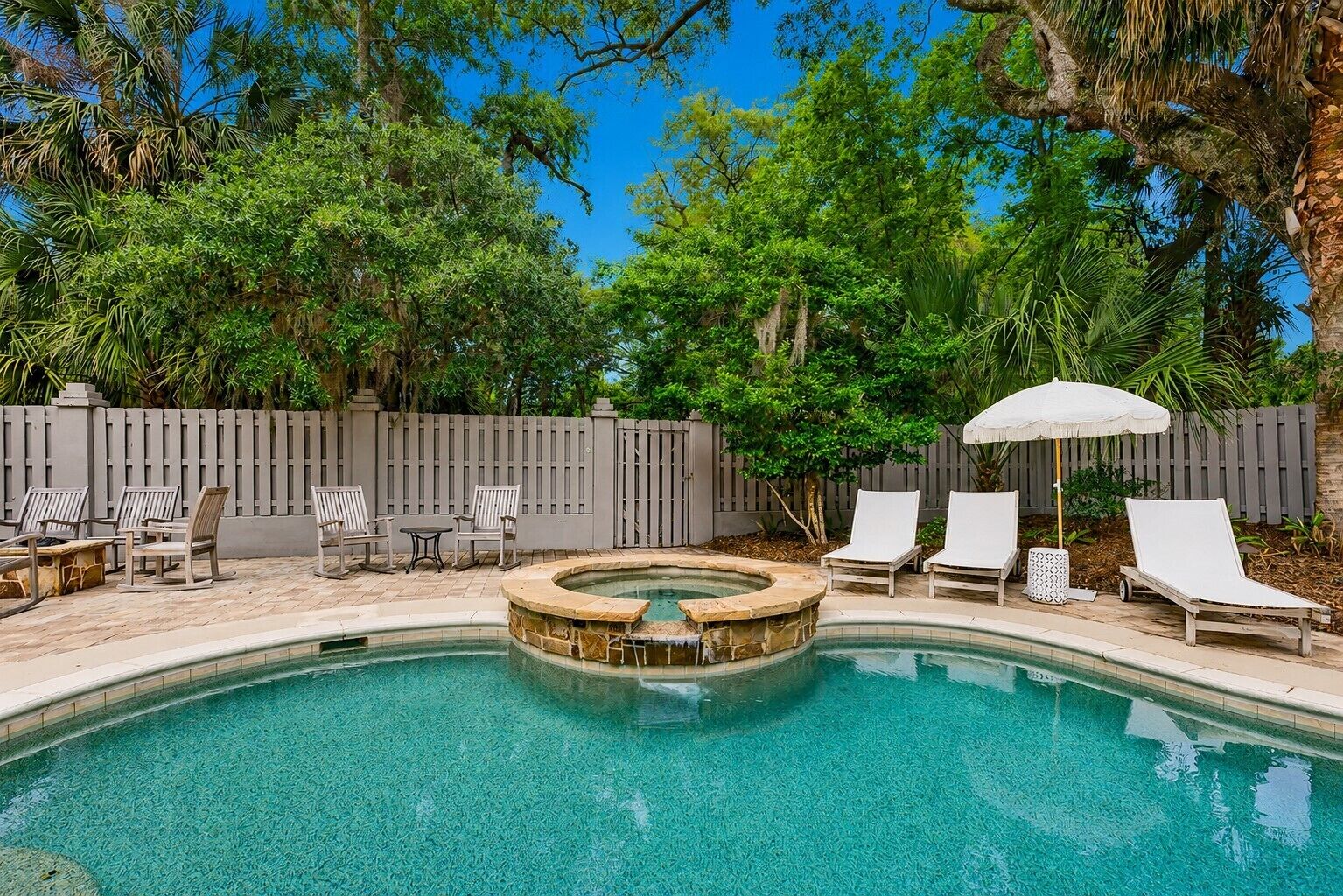 A swimming pool with a hot tub, surrounded by lounge chairs and a wooden fence.