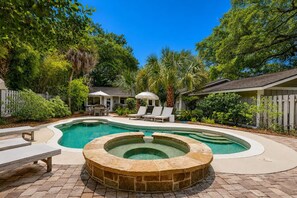 A backyard with a swimming pool, a hot tub, and a patio area with lounge chairs and a table.