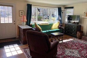Cozy living room with a sofa, armchair, and coffee table, featuring a fireplace and large window.