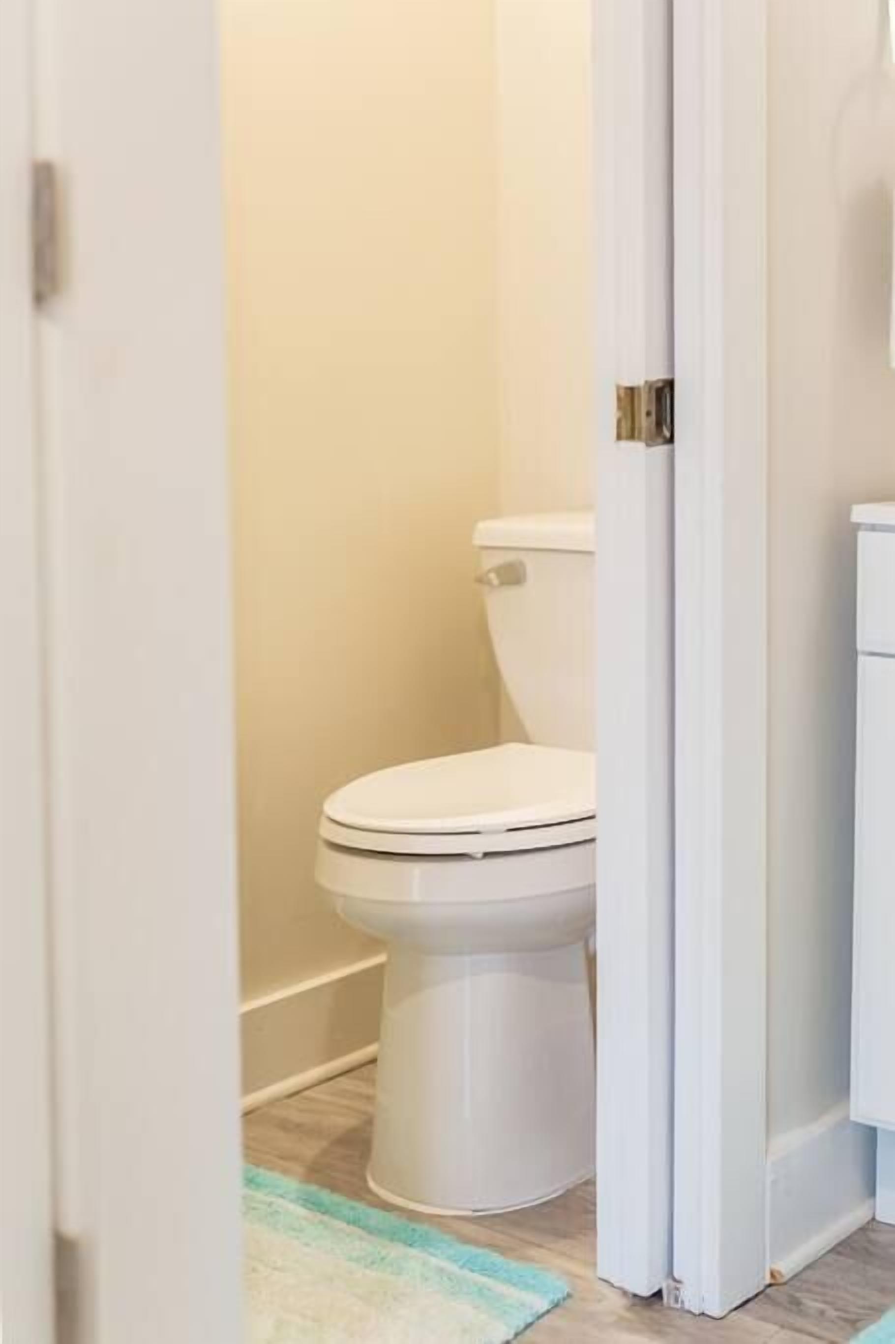 Une salle de bain avec des toilettes blanches, un mur de couleur beige et un plancher en bois.