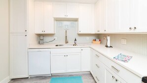 A kitchen with white cabinets, a dishwasher, a sink, and a countertop with a towel and a soap dispenser.